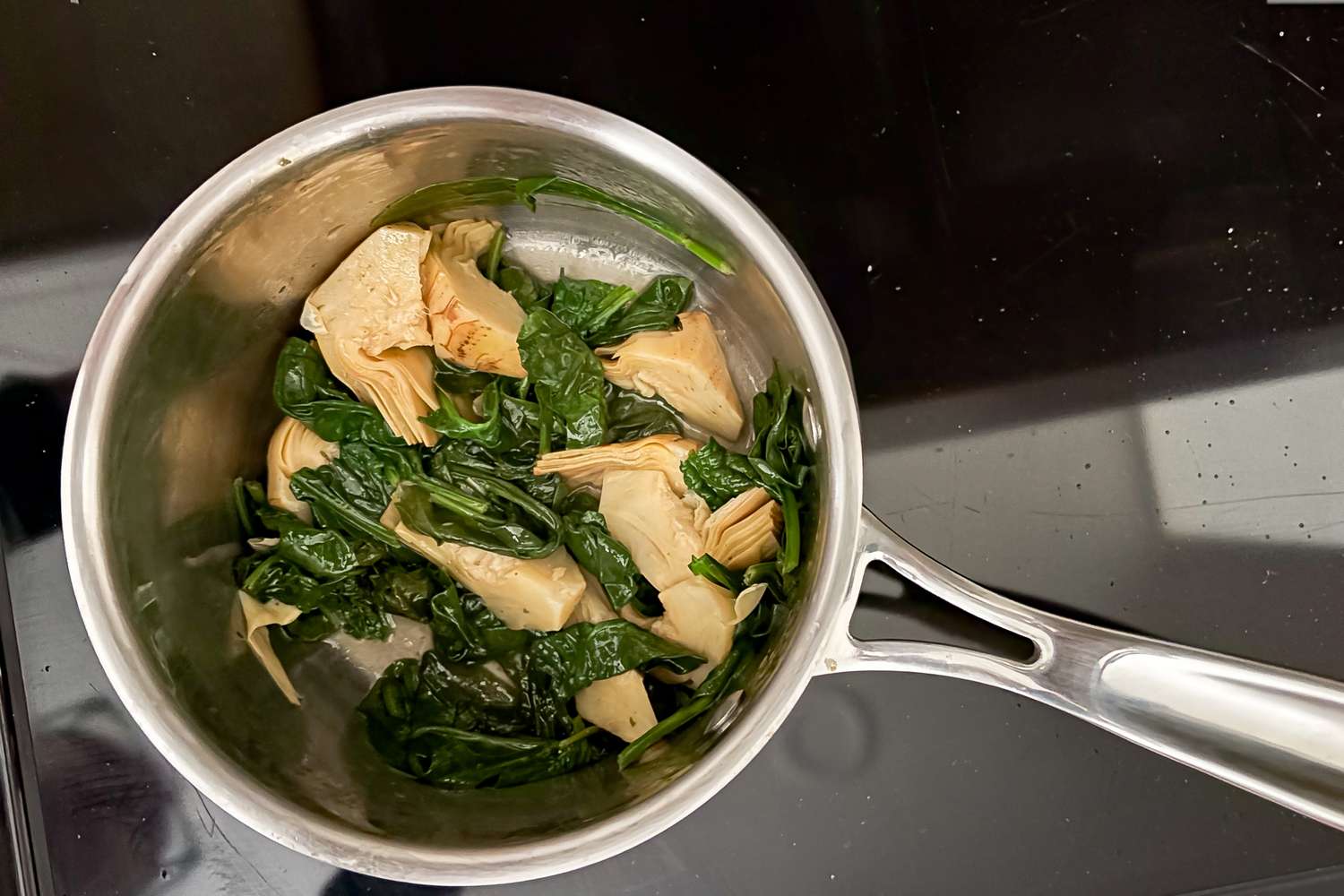 A saucepan containing cooked spinach and artichoke hearts for Ree Drummond’s 4-Ingredient Artichoke Dip