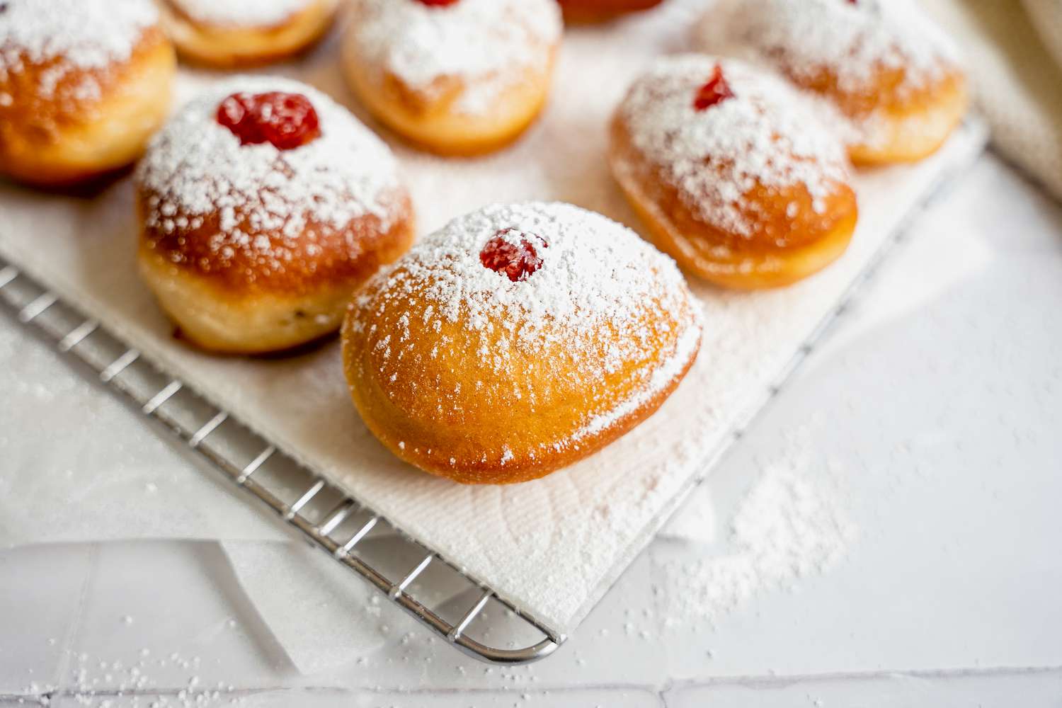 Sufganiyot (Israeli Jelly Donuts) on a Paper Towel Lined Cooling Rack Sitting on Parchment Paper