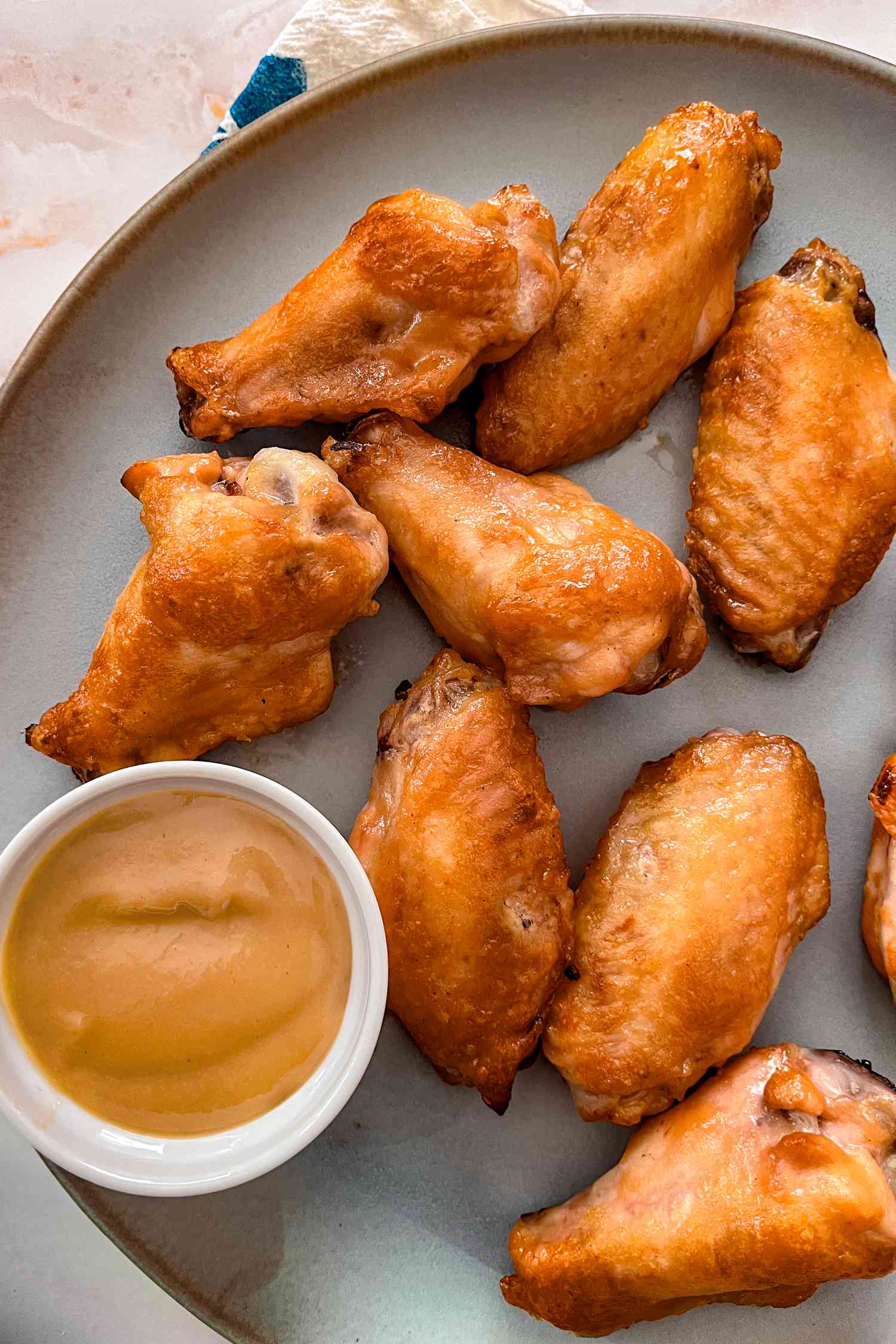 Overhead view of a gray plate of chicken wings with a small bowl of honey mustard for dipping