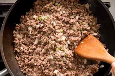 Cooking ground beef with diced onions in a skillet a wooden spoon stirring the mixture