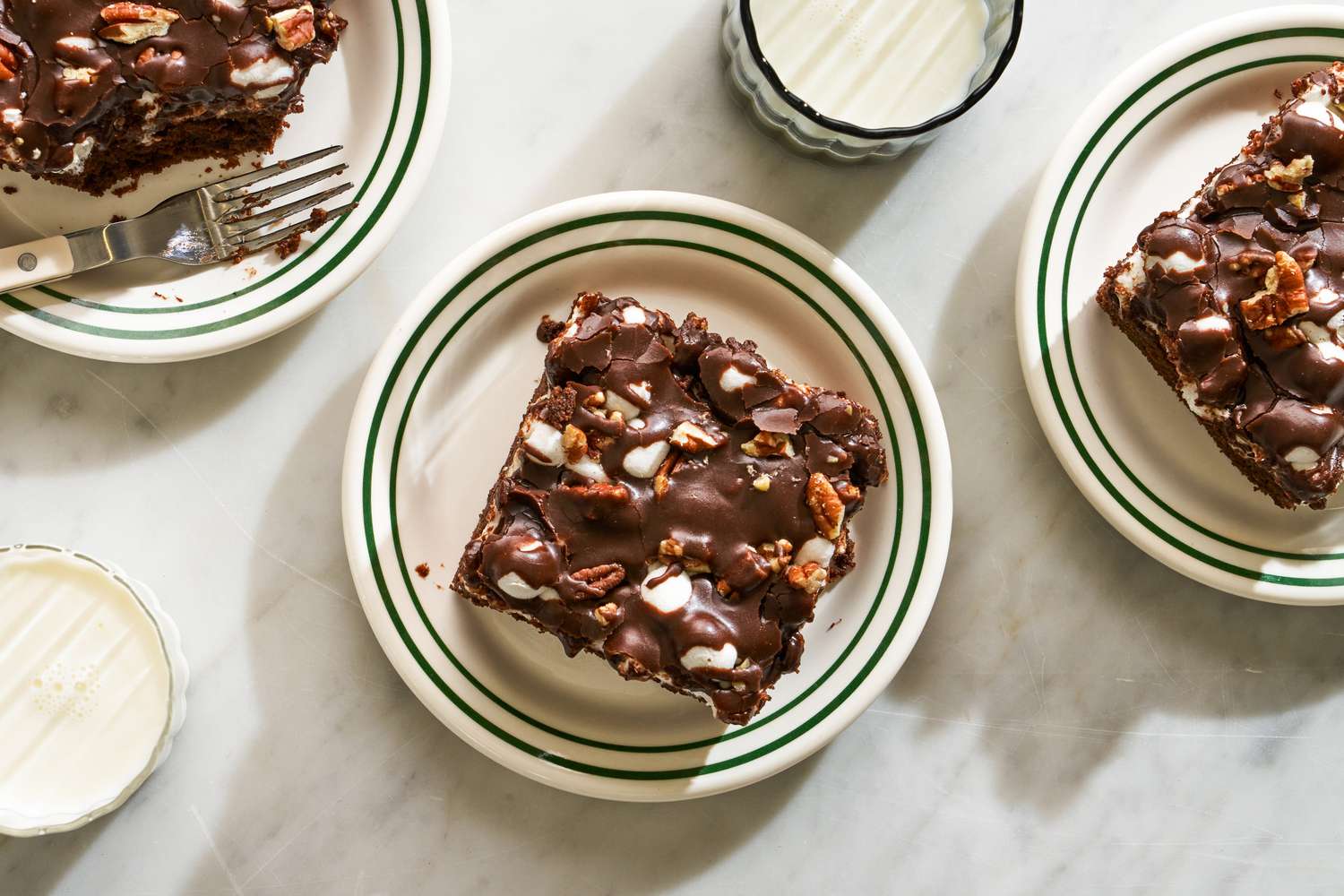 Overhead view of three plates each containing a slice of Mississippi Mud Cake next to two glasses of milk