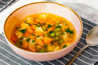Bowl of vegetable soup with carrots peas and herbs on a striped cloth