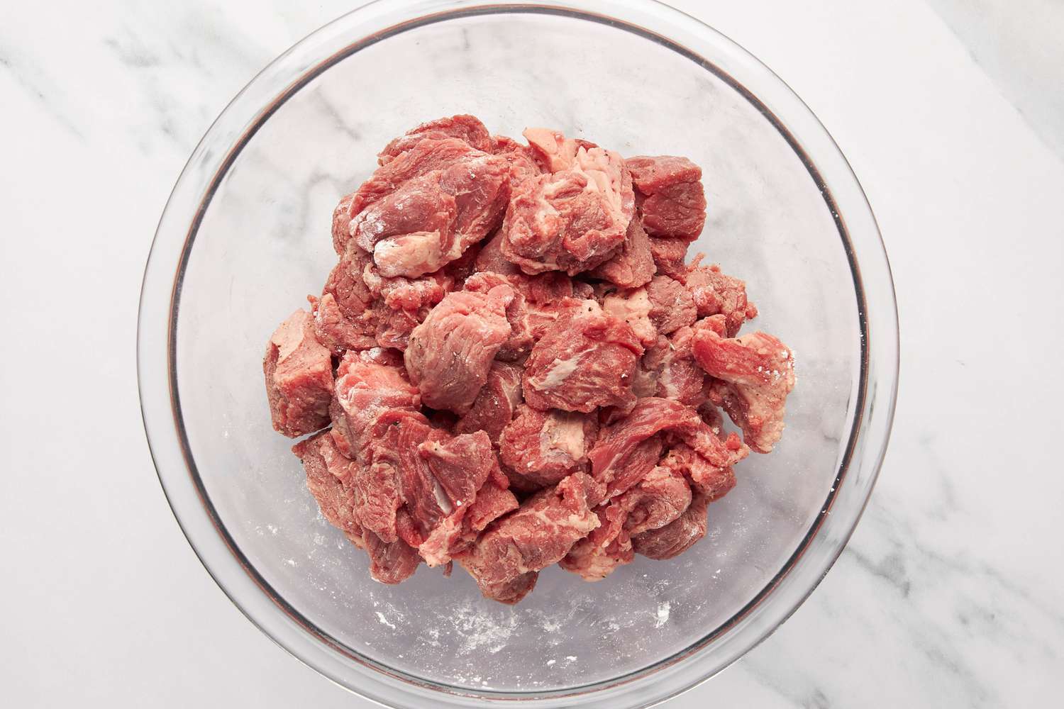Chuck roast coated in flour, salt, and pepper in a bowl for carne picada recipe