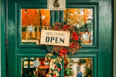 Green door for a store with a wreath and an open sign hanging on the front