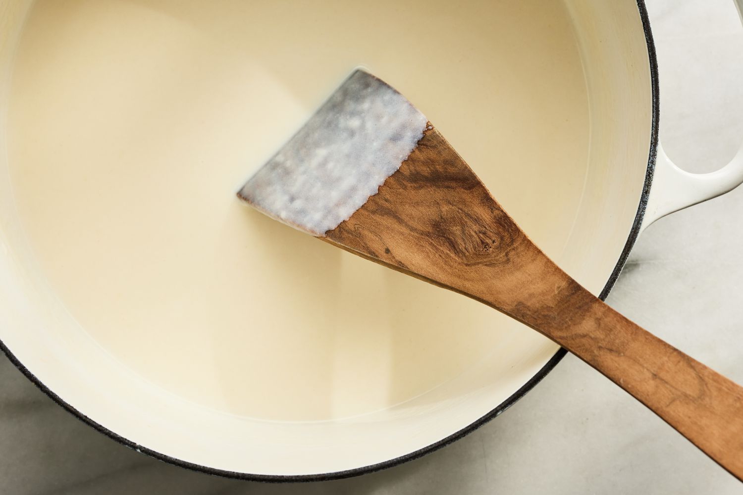 Overhead view of a white dutch oven while mixing the flour, butter, milk and cream ingredients with a wooden spoon for Million Dollar Mac and Cheese recipe