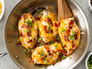 Cooked chicken breasts with cheese, bacon, and green onion in a pan