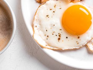 Close up of a sunny side up egg on a plate with a mug of coffee peeking in