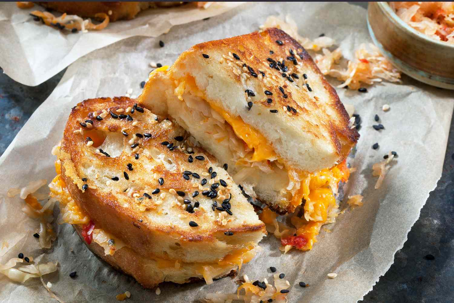 Kimchi grilled cheese sandwich cut in half topped with sesame seeds and served on parchment paper