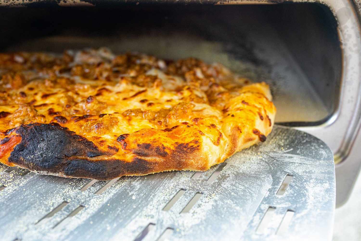 Easy pizza with sausage being taken out of the Roccbox using a pizza peel.