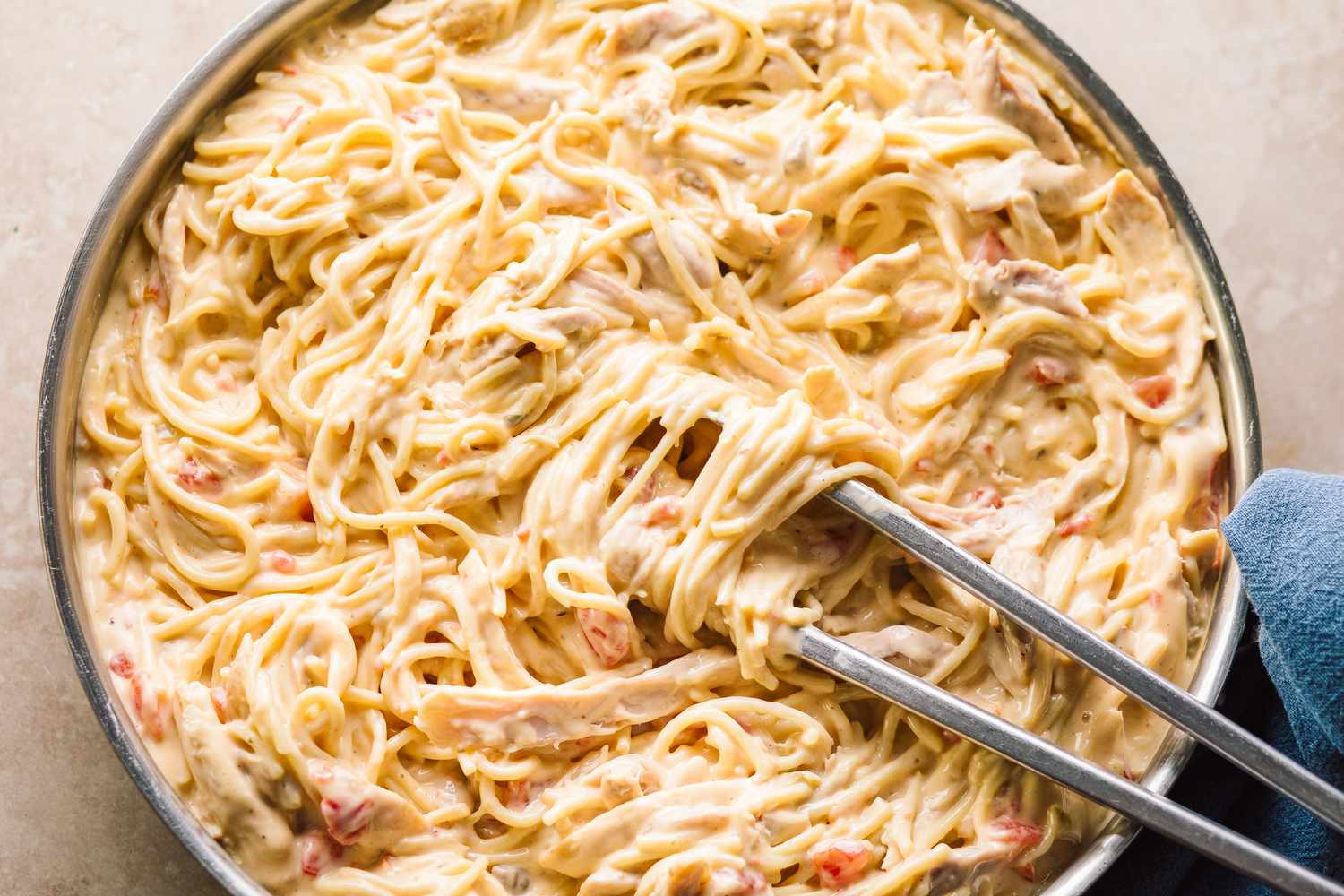 close up view of Chicken Queso Spaghetti in a pan with tongs