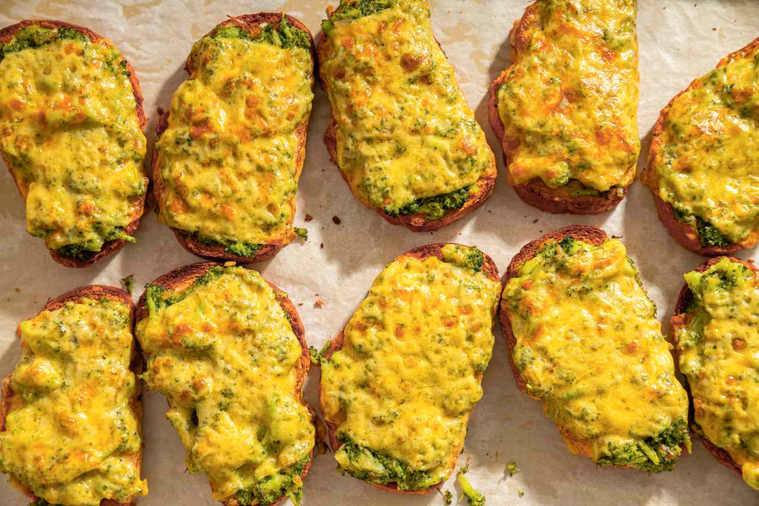 Broccoli and cheddar cheese toasts arranged in rows on a baking sheet