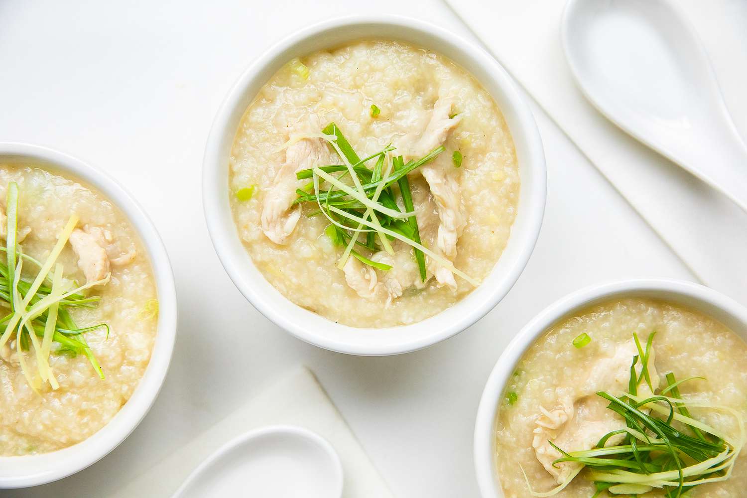 Bowls of Chicken Congee Topped with Sliced Ginger and Green Onions, Next to Soup Spoons
