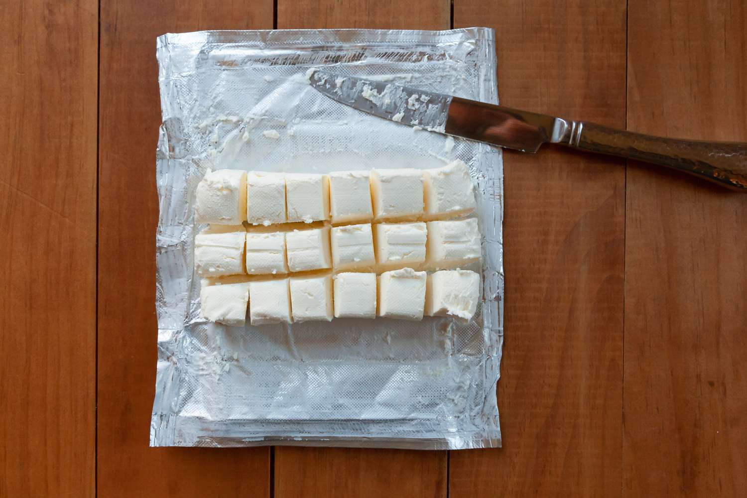 A block of cream cheese cut into squares to make a whipped cream frosting recipe.