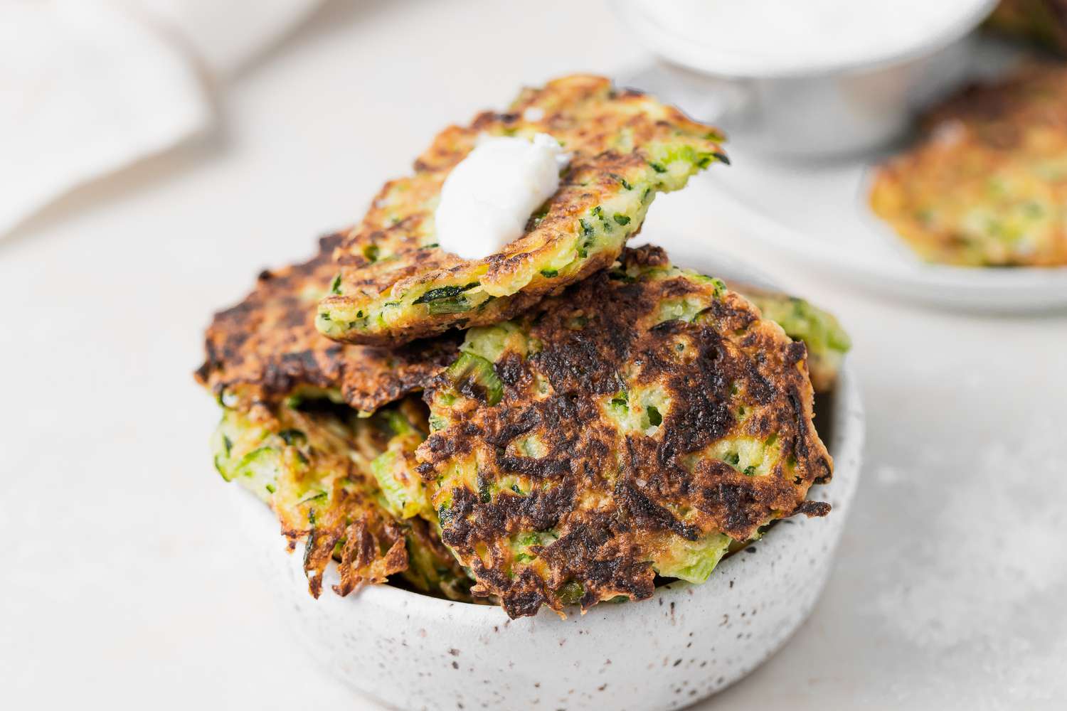 A bowl of zucchini fritters set on a white background.