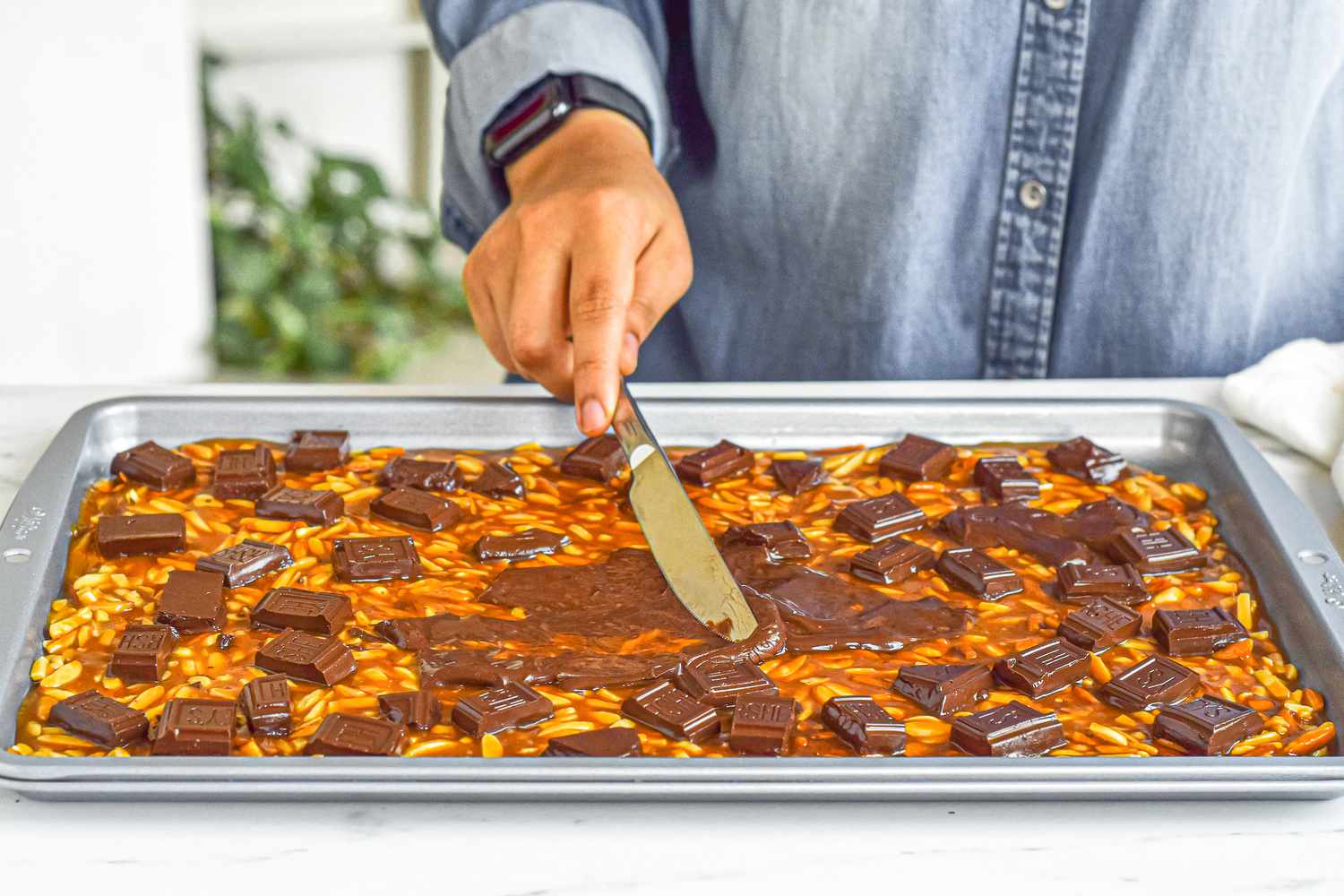 Spreading melted chocolate over almond roca.
