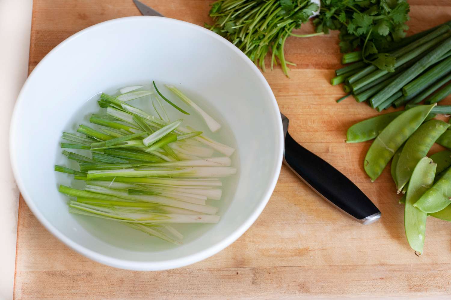 Sliced scallions set in cold water to make a vegetarian rice noodle salad.