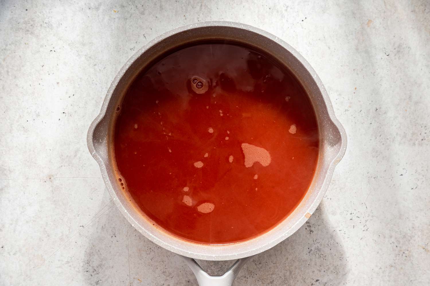 Tomato broth heating up in a saucepan for assassin's spaghetti recipe