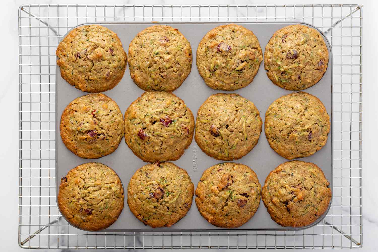 Overhead view of a muffin tin of zucchini bread muffins cooling on a rack.