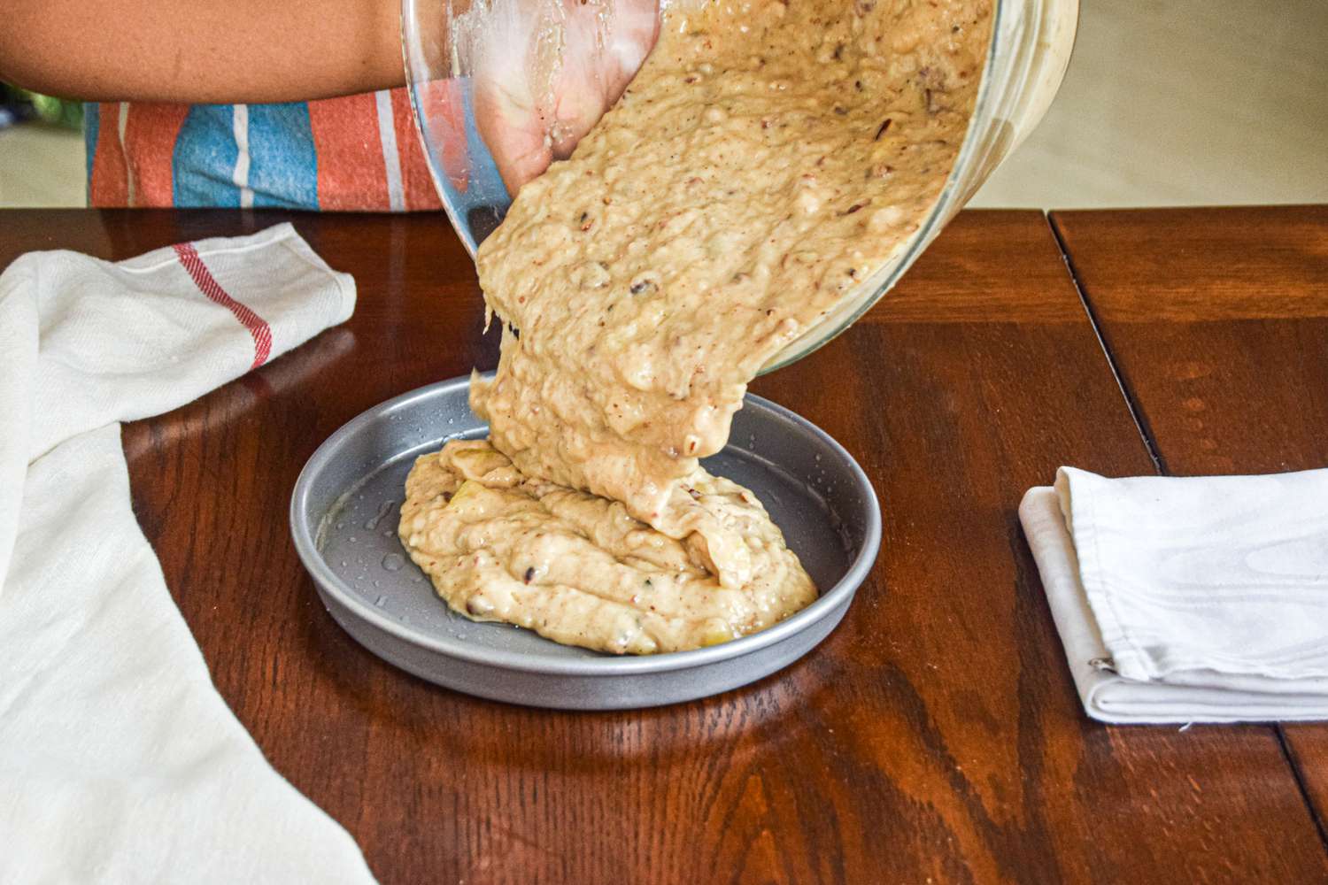 Pouring batter into a cake pan to make a hummingbird cake.
