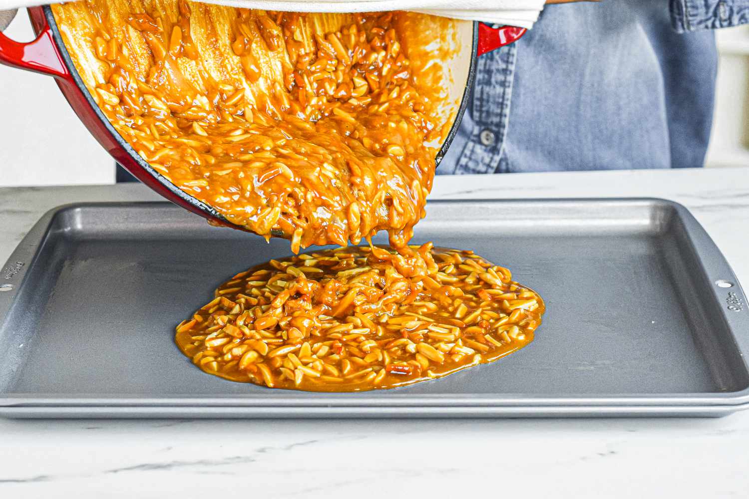 Pouring almond roca onto a baking sheet.