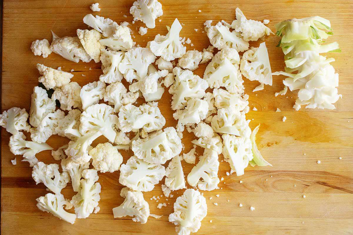Chopped raw cauliflower on a wooden cutting board.