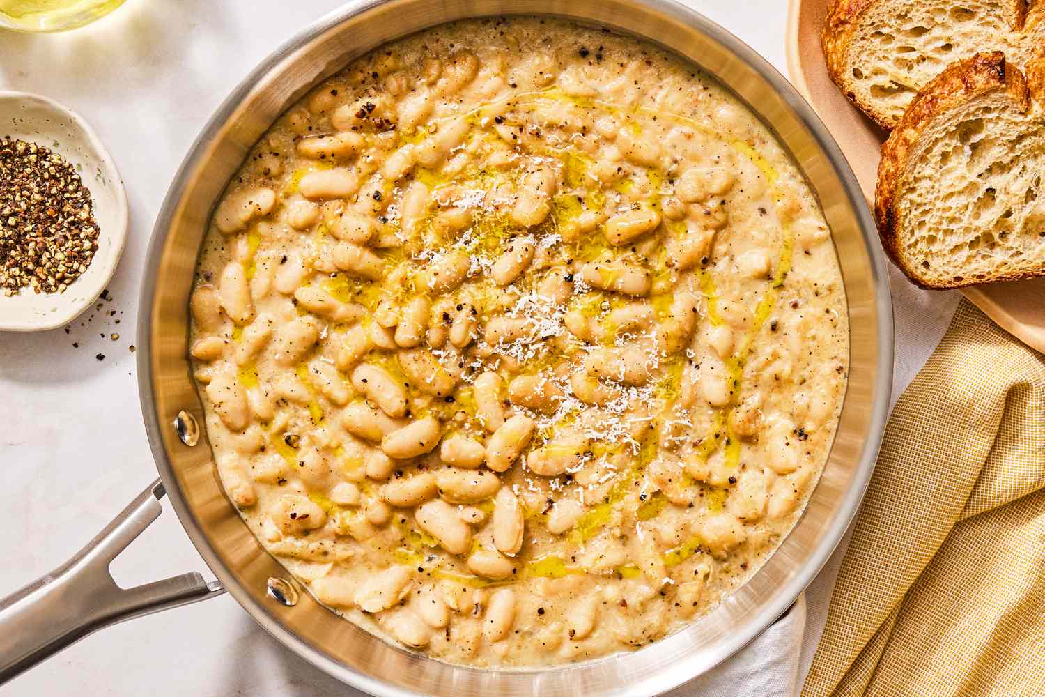 A dish of creamy cacio e pepe beans garnished with grated cheese and served with bread
