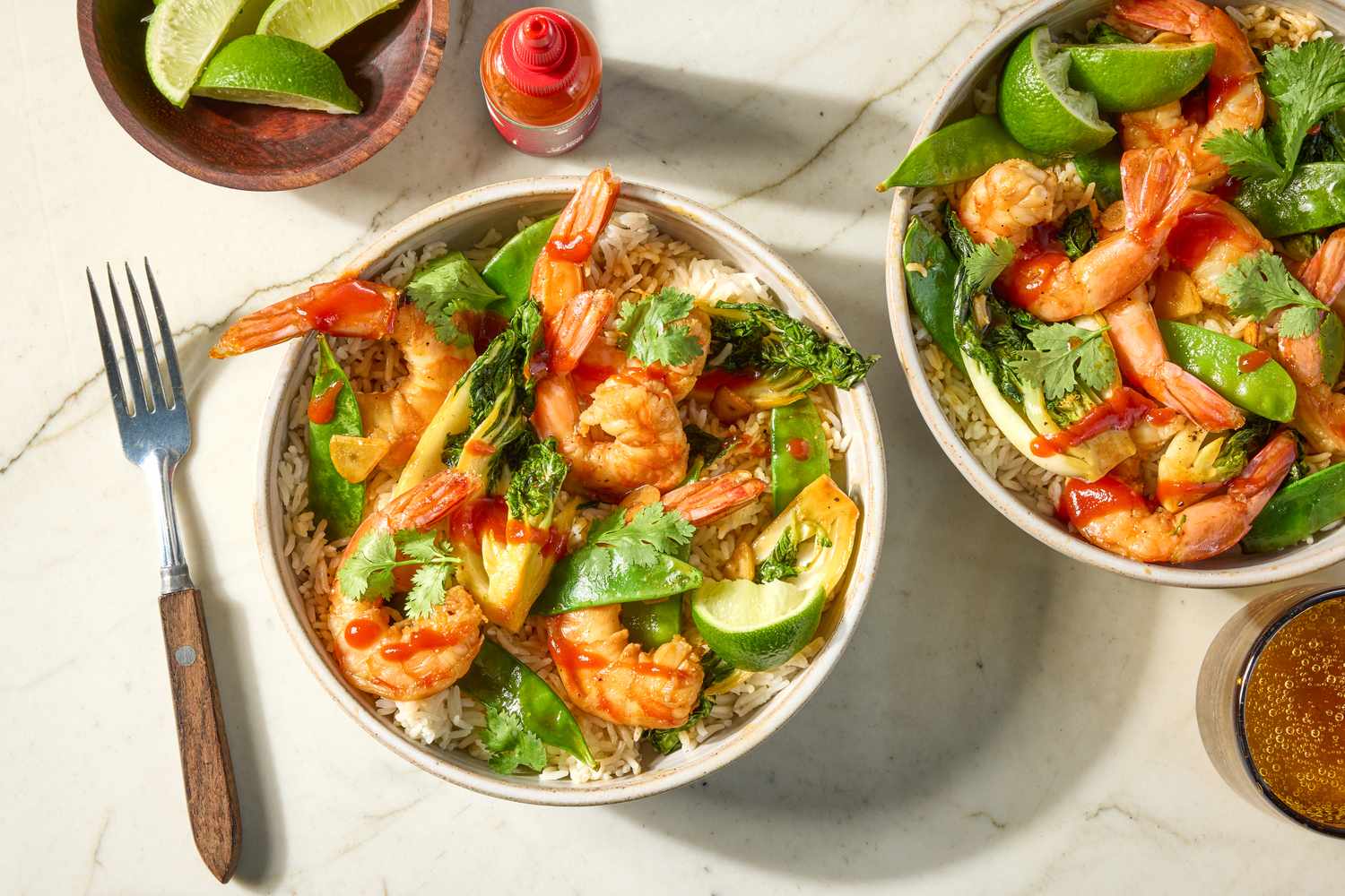 Shrimp Stir Fry in bowls over rice, hot sauce and lime wedges on the side