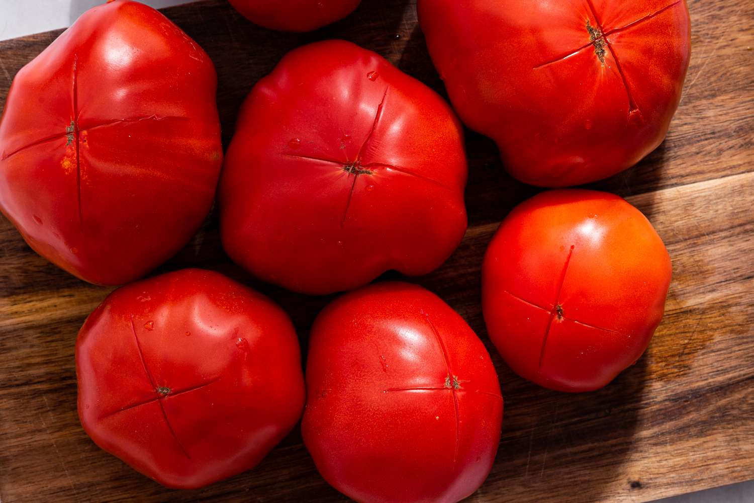 Tomatoes with shallow cross cuts on the bottom, all on a wooden cutting board for bruschetta with tomato and basil recipe
