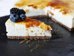 Vanilla Bean Cheesecake with brittle sugar topping on a slate board wtih a slice cut out and fruit nearby.