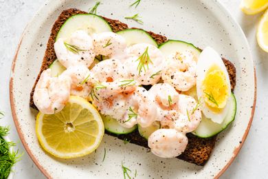 Scandinavian Shrimp Sandwich on a plate, garnished with wedge of a boiled egg, chopped fresh dill, and a lemon slice