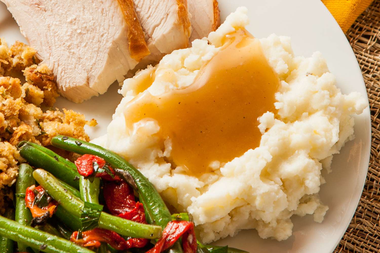 Plate of thanksgiving dinner: slices of turkey, stuffing, green beans and roasted bell peppers, and a mashed potatoes with gravy