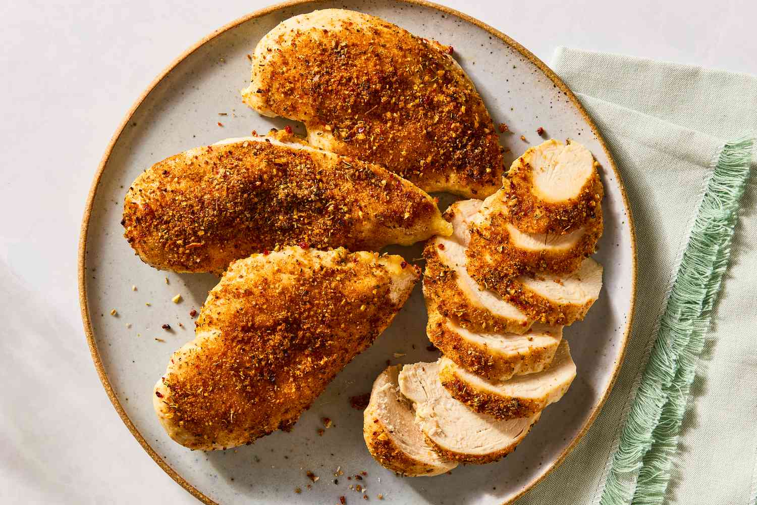 Overhead shot of a plate with three seasoned whole chicken breasts an one sliced chicken breast