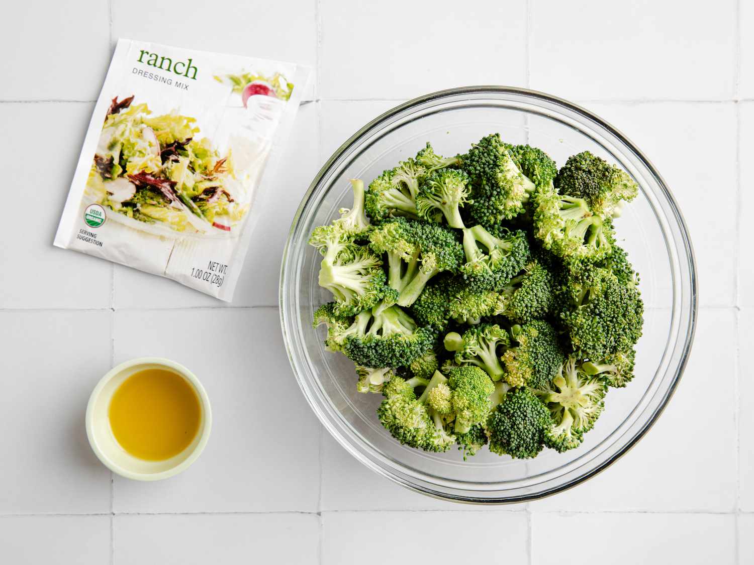 view from above of a bowl of broccoli, a ranch seasoning packet, and a small bowl of oil