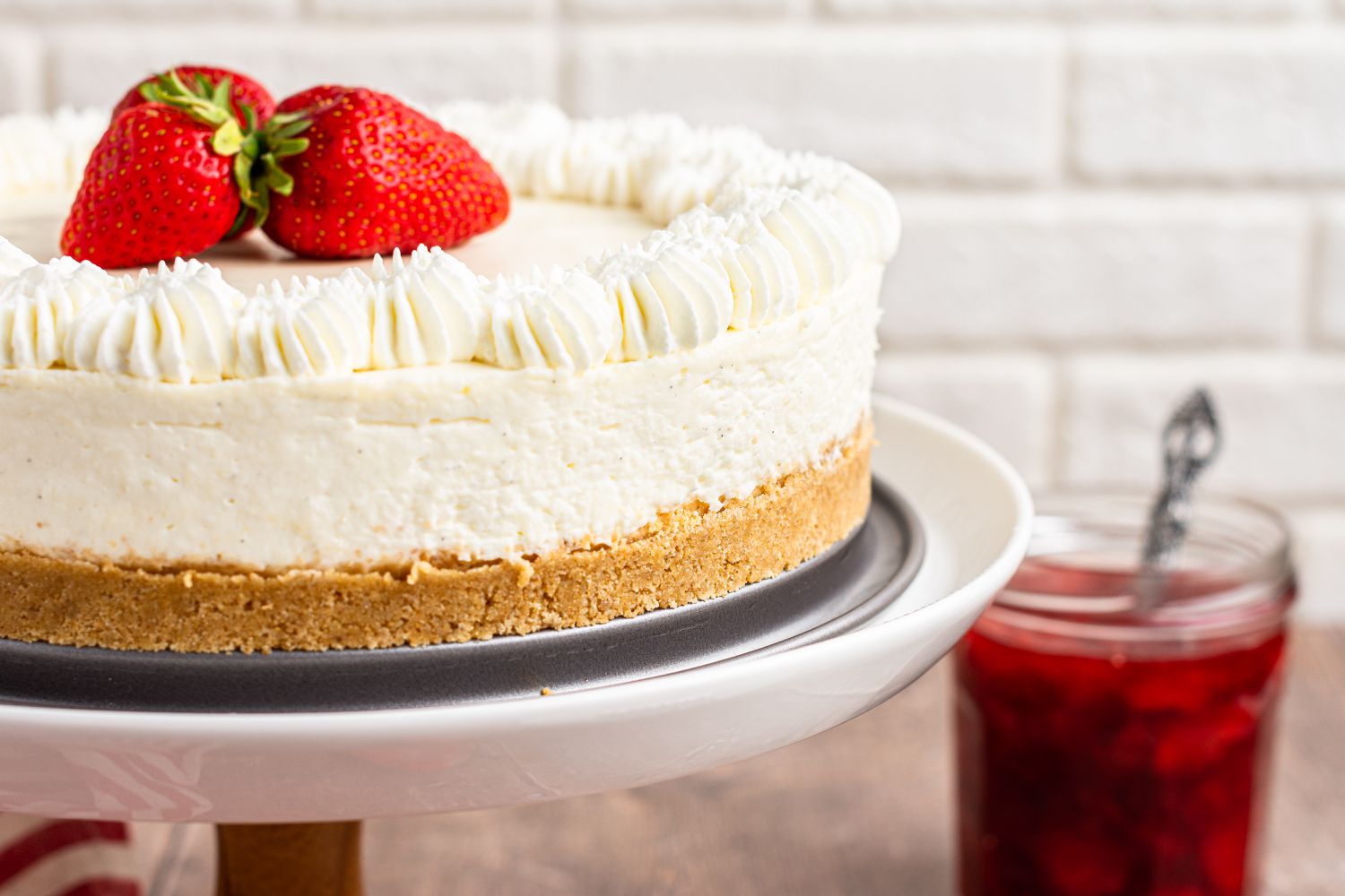 Side view of a A cake stand with no bake cheesecake topped with fresh strawberries.