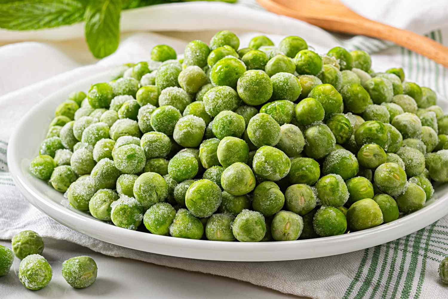 A plate of frozen green peas on a striped dish towel