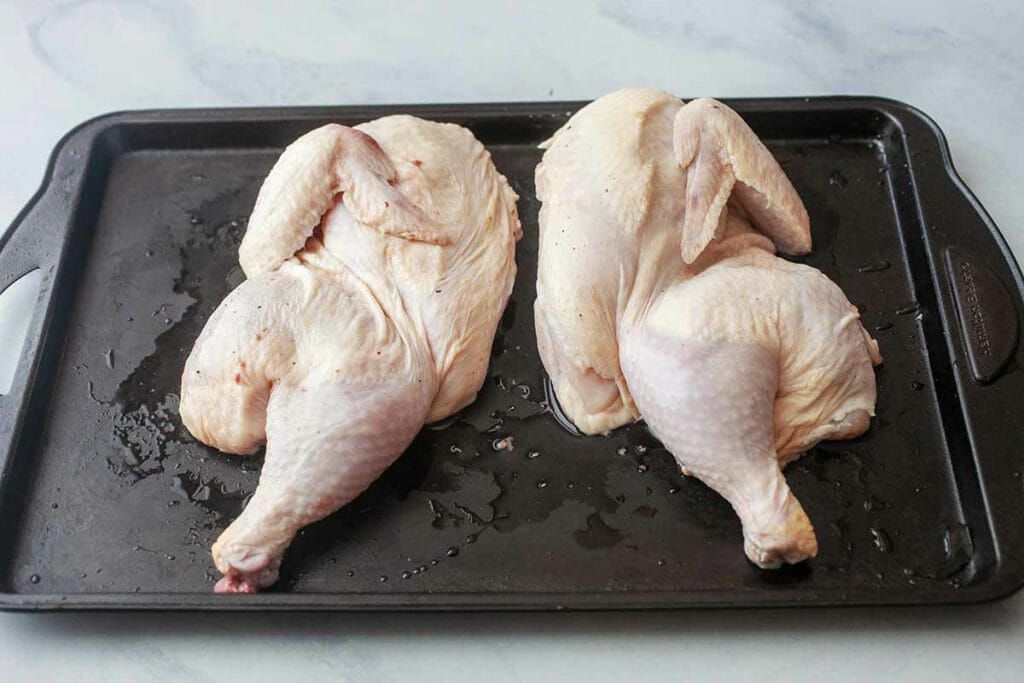 Raw butterflied chicken on baking sheet for chicken under a brick