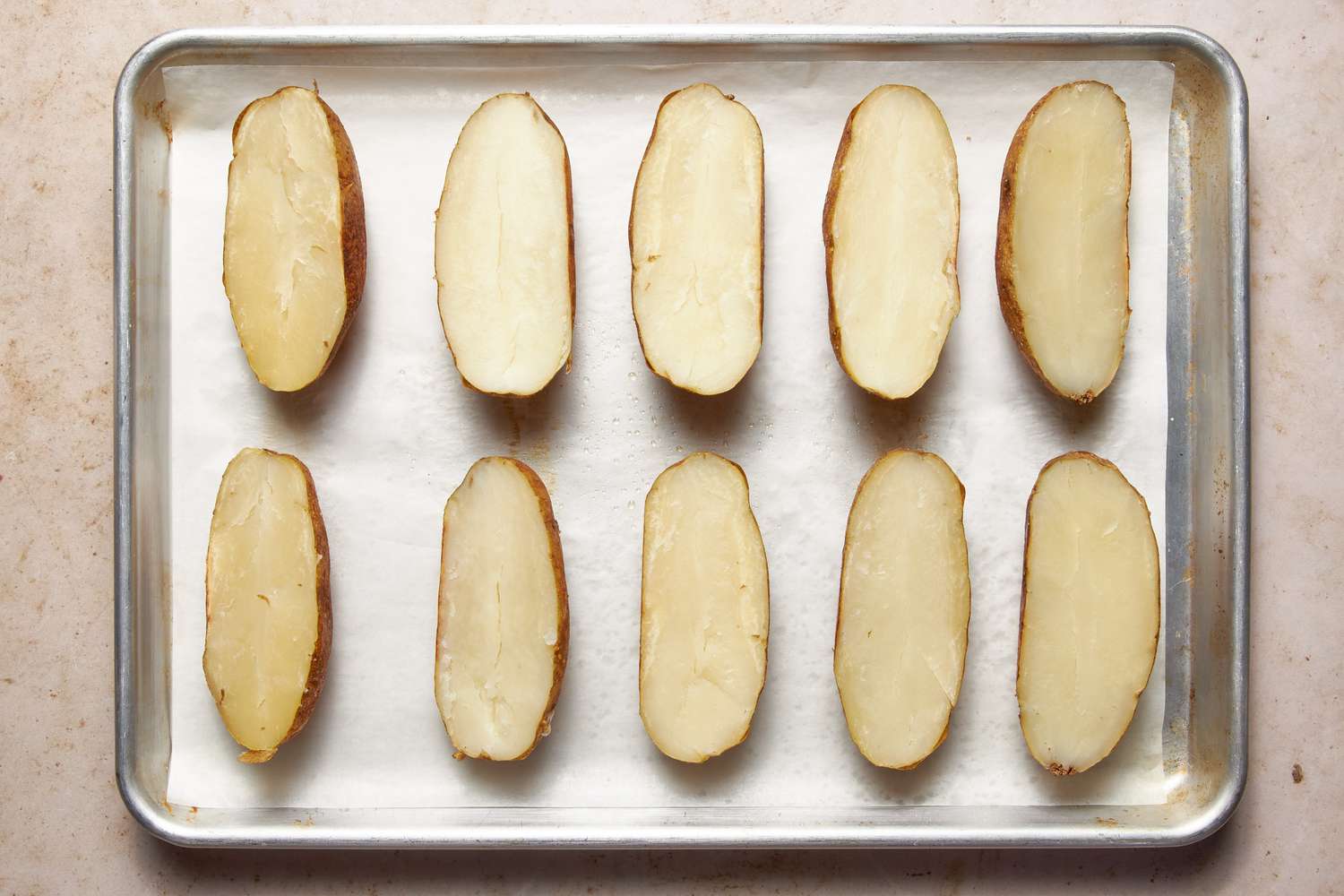 Baked potatoes cut in half and resting on a parchment paper-lined baking sheet for twice baked potatoes recipe