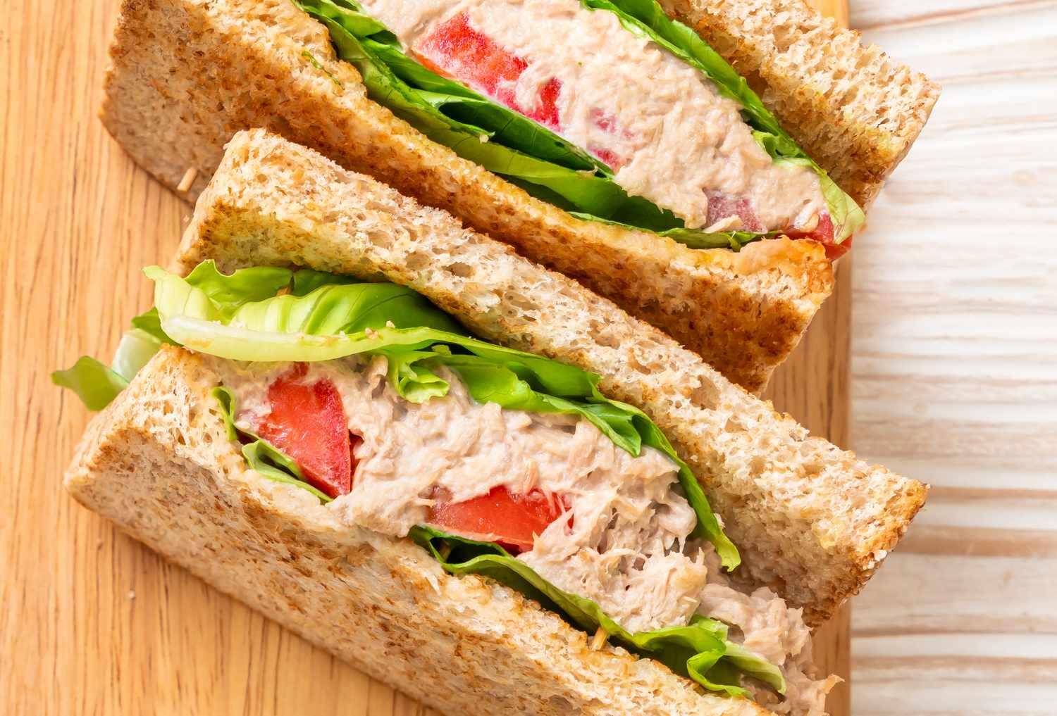 Tuna sandwich with lettuce and tomato slices on whole grain bread sliced diagonally