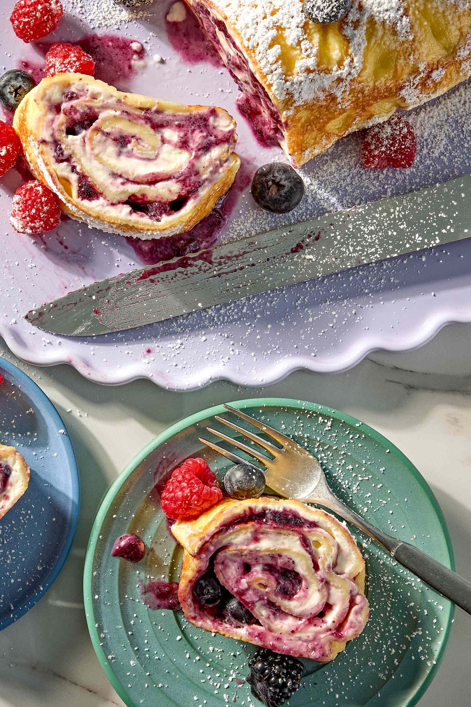 Sliced crepe cake filled with fruit compote dusted with powdered sugar served with berries on plates