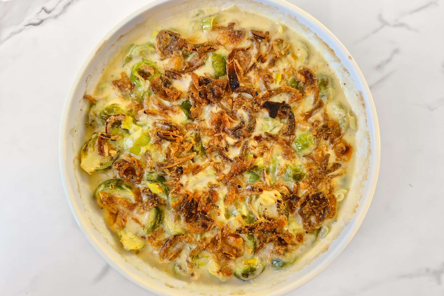 Cooked Brussels sprouts in a creamy sauce topped with crispy caramelized onions served in a circular baking dish