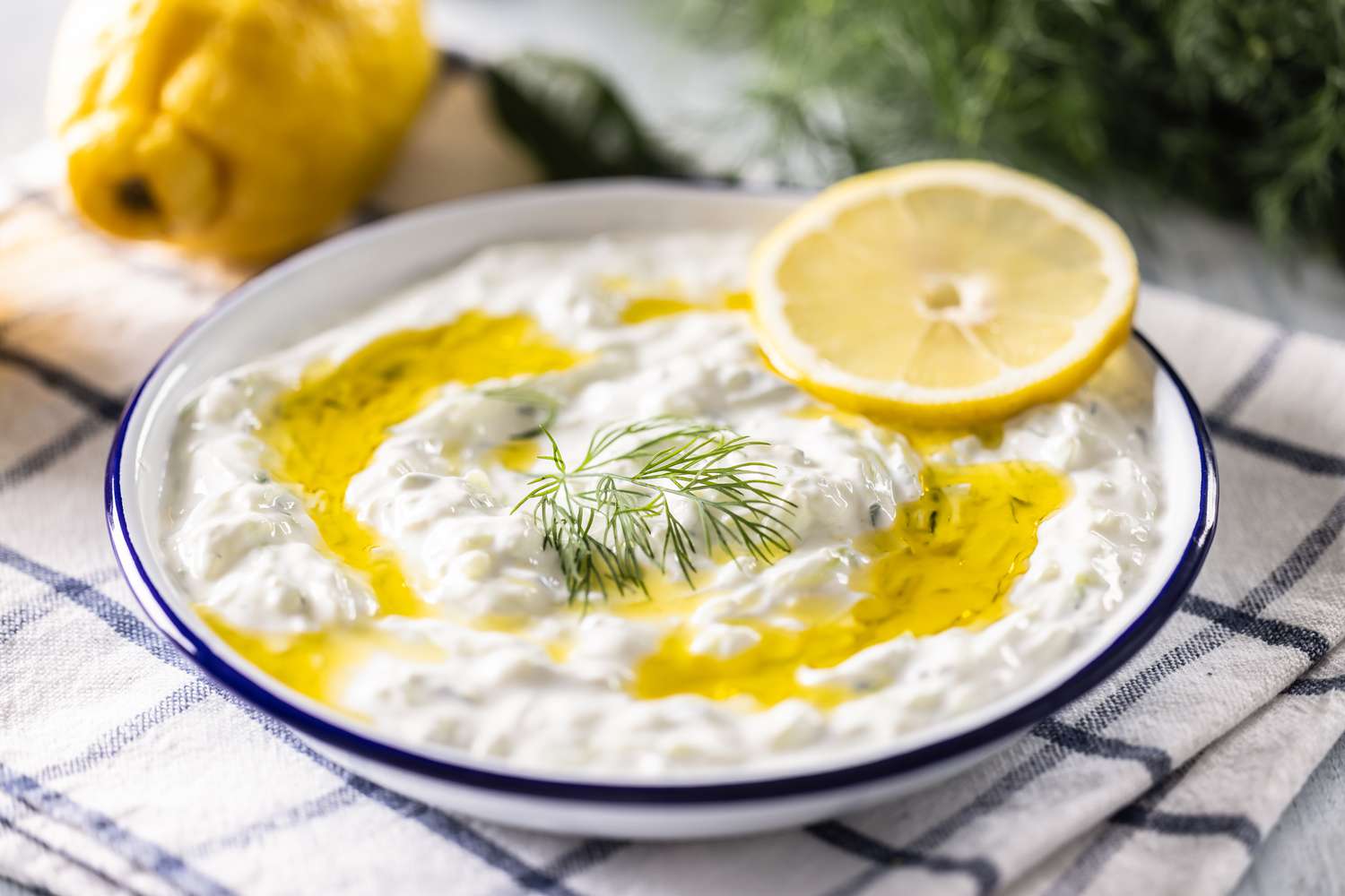 A bowl with tzatziki, garnished with fresh dill and a lemon wheel