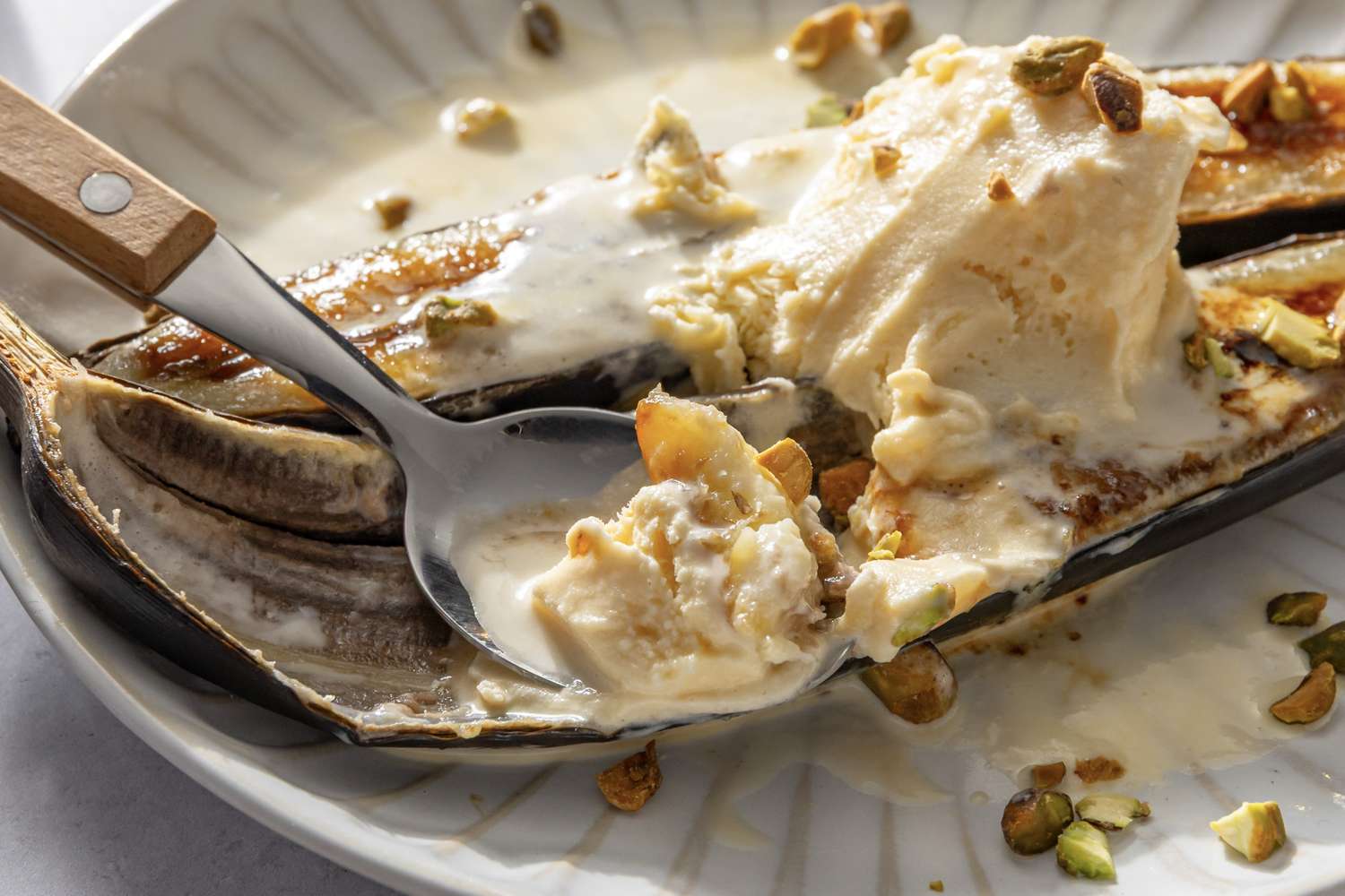 Caramelized bananas topped with ice cream and chopped nuts on a plate with a spoon