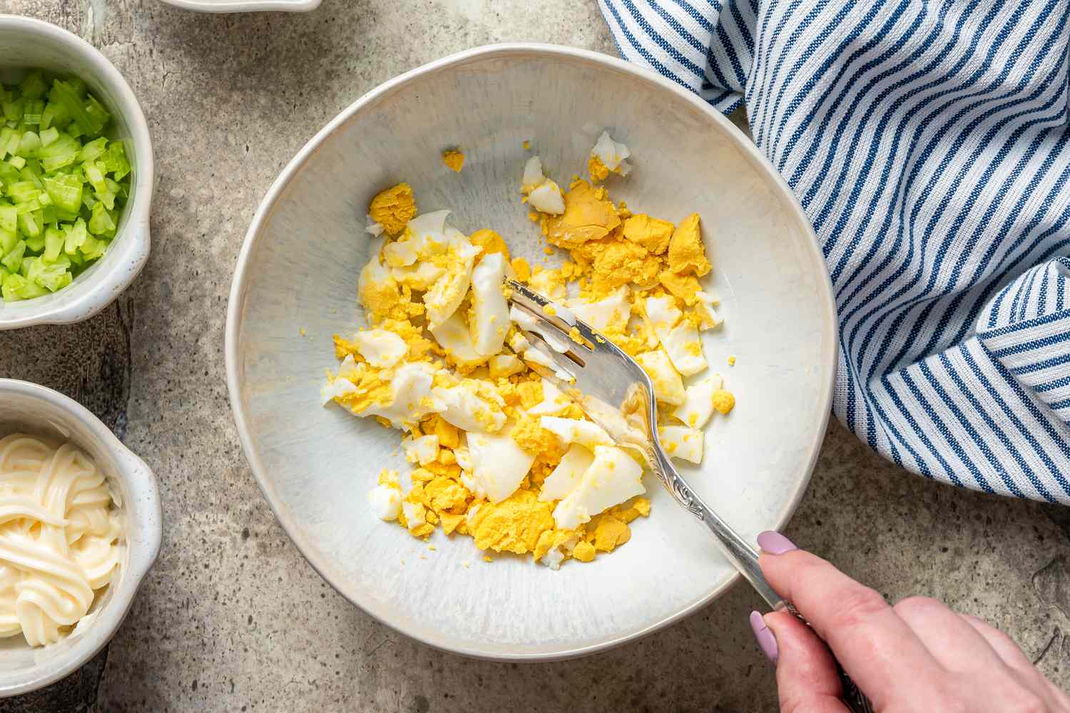 Smashing hard boiled eggs in a bowl to learn how to make egg salad