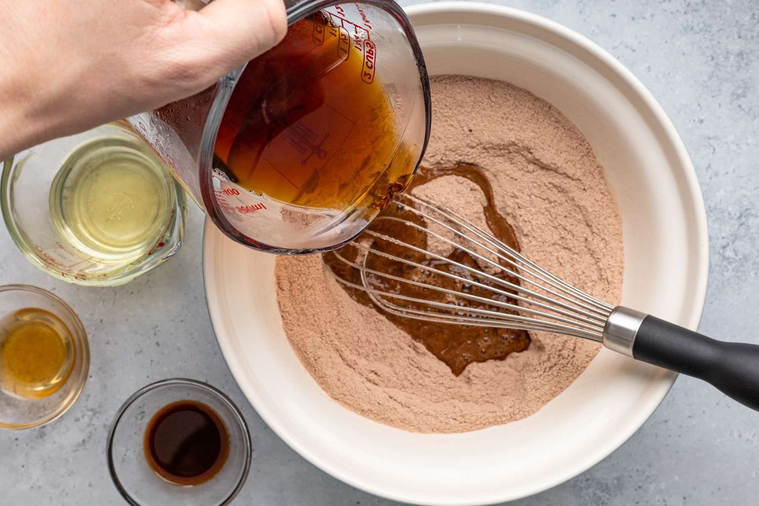 Brewed Coffee Poured into Bowl of Dry Ingredient, and Next to It, Small Bowls and Pyrex Measuring Cups With the Rest of the Wet Ingredients for One-Bowl Chocolate Cake Recipe