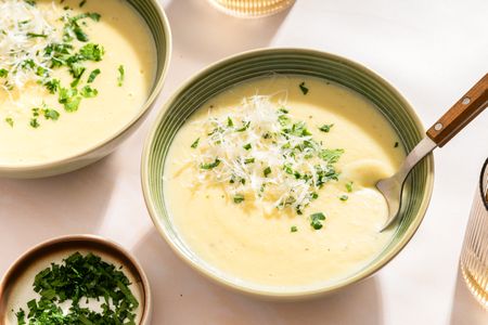 Bowls of potato soup garnished with parsley and grated cheese on a table