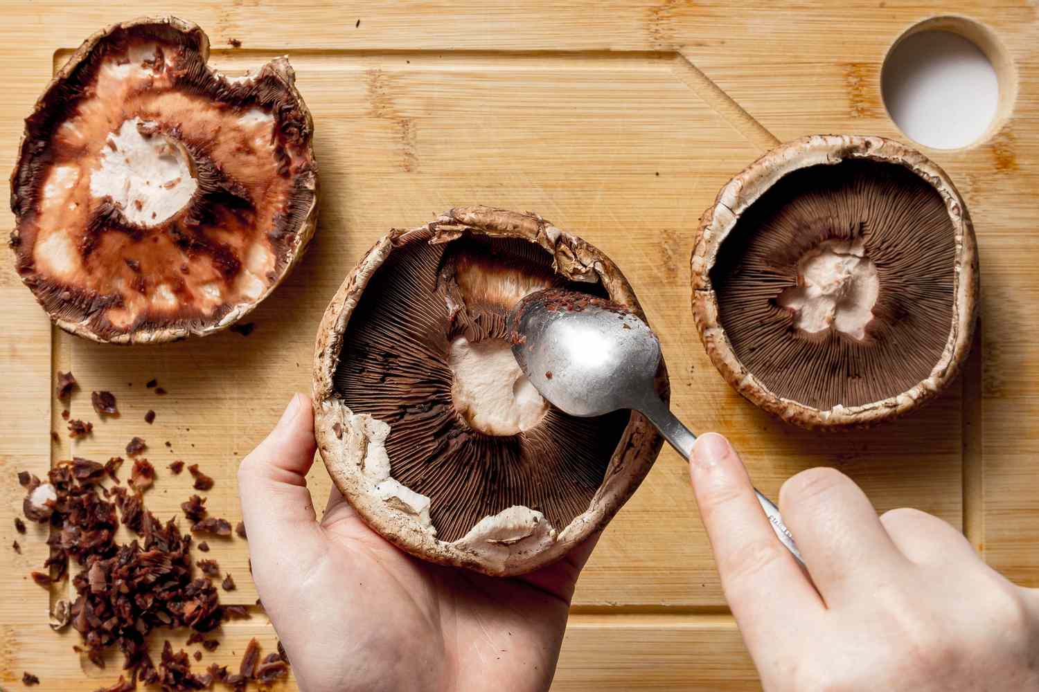 Portobello Mushroom Gills Removed Using a Spoon, and on the Cutting Board Below, One Mushroom With Gills Removed and Another Still Intact