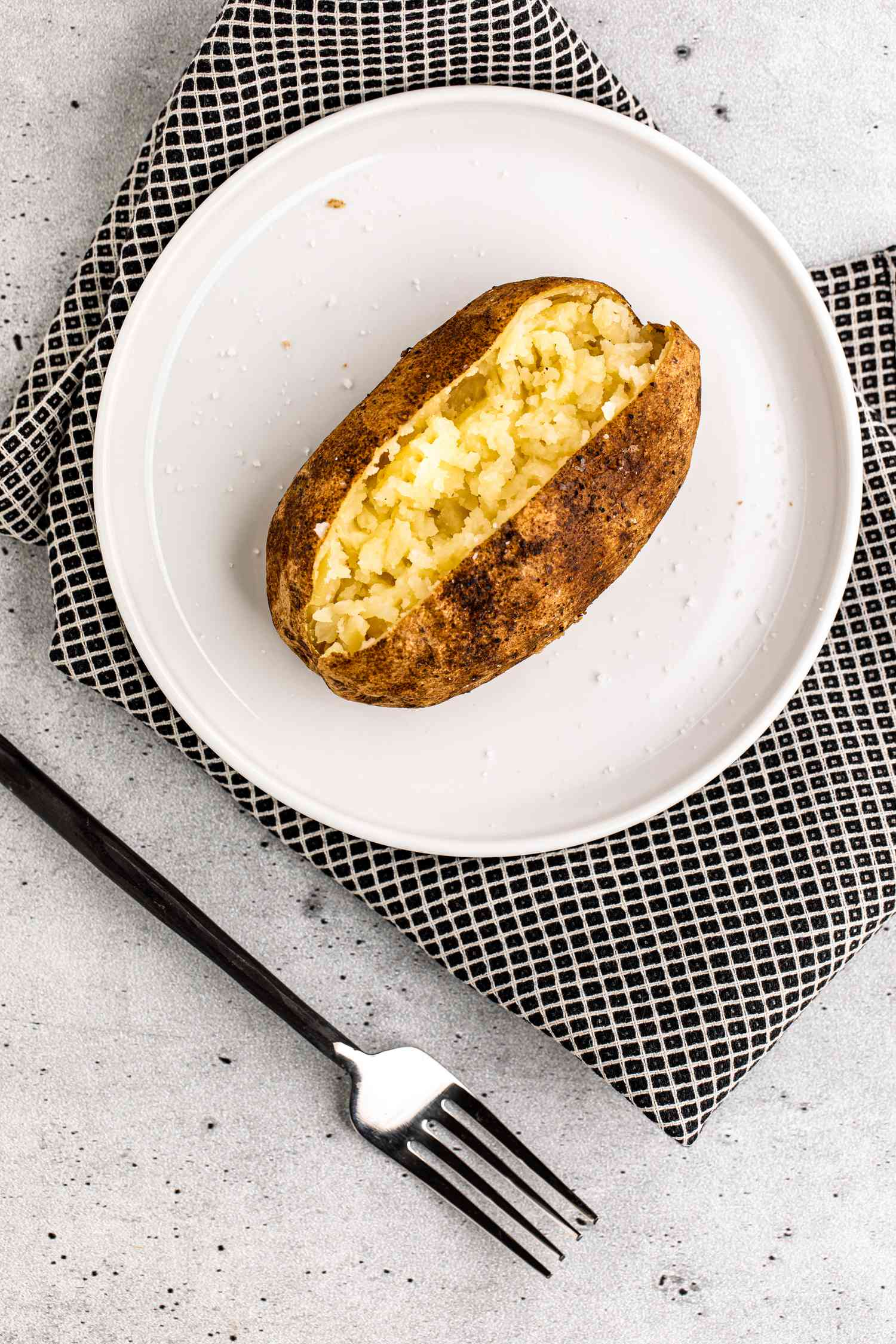 Grilled Baked Potato on a Plate over a Napkin and Next to a Fork