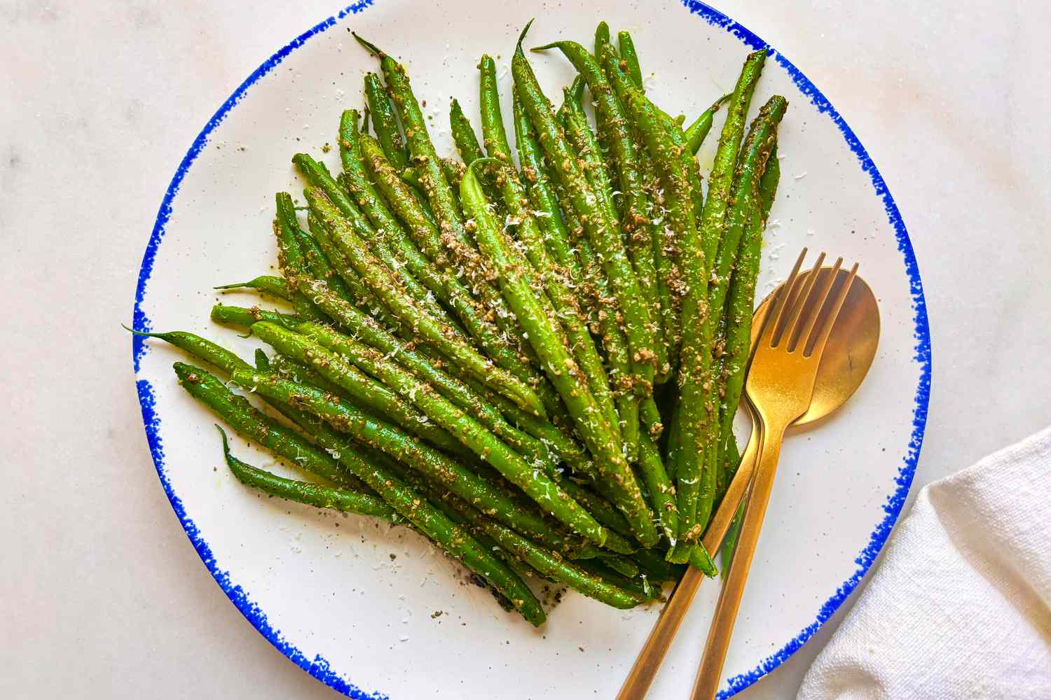 Plate of green beans on a white plate with golden utensils, sprinkled with seasoning