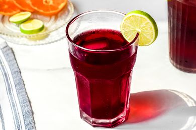 Agua de Jamaica (Hibiscus Tea) Served with Ice and a Lime Slice Next to a Small Plate of Sliced Oranges and Limes and a Pitcher with More Jamaica