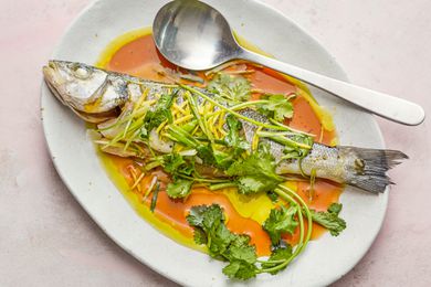Overhead view of a steamed whole fish on a flatter and topped with sauce and herbs.